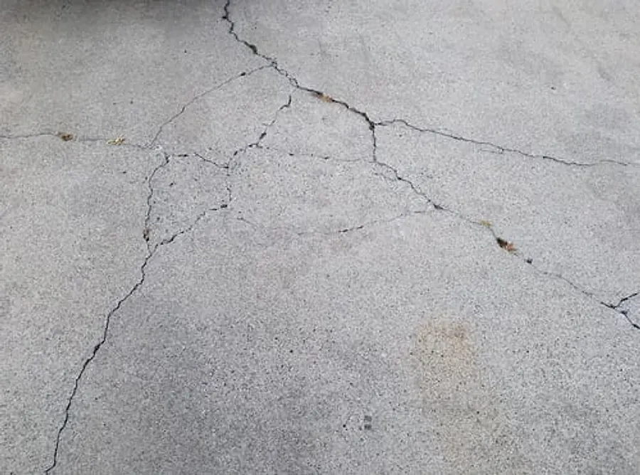 Network of shrinkage and settlement cracks spreading across a weathered gray concrete slab